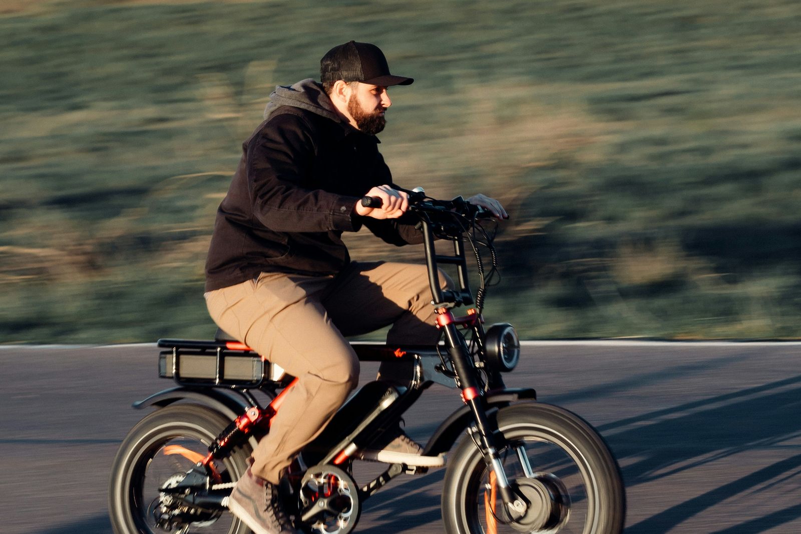 A rider on a fat-tyre e-bike moving fast along an open road in low evening sun