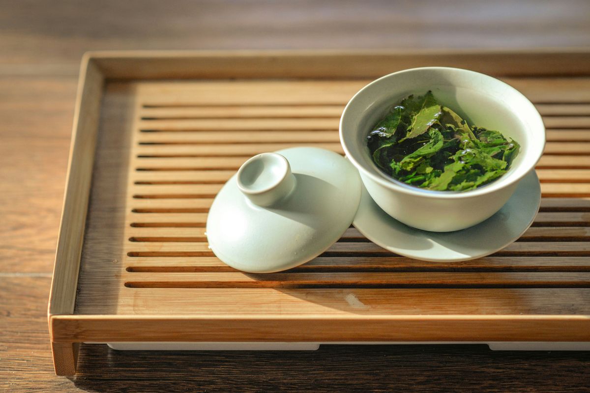 Rolled tea leaves opening in a pale celadon gaiwan on a bamboo tea tray