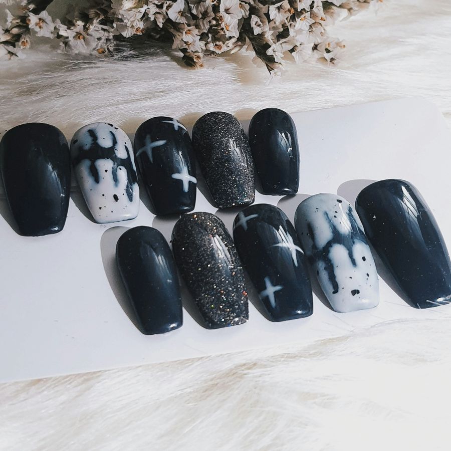 A full set of black coffin press-on nails with glitter, white drips and star details