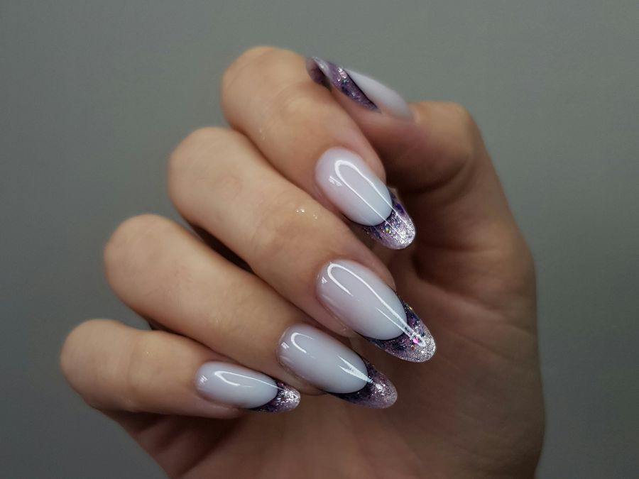 A hand wearing long almond nails in milky white with lilac glitter French tips